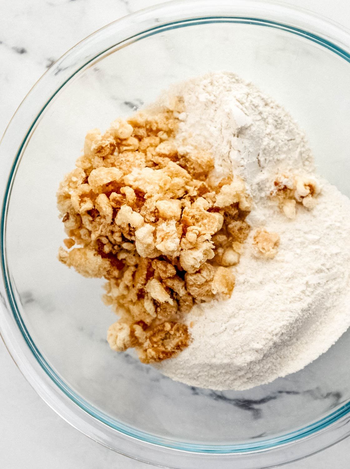 Overhead view of cornmeal, flour, and cracklin in a large glass mixing bowl. 