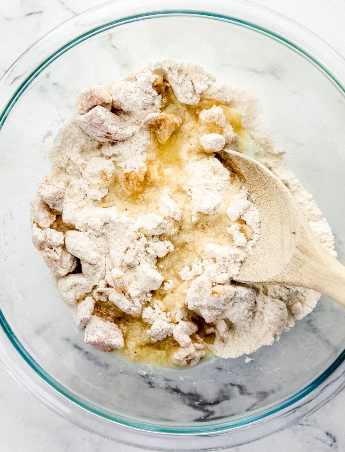 Melted butter added to the flour, cornmeal, and cracklin in a large glass mixing bowl with a wooden spoon. 