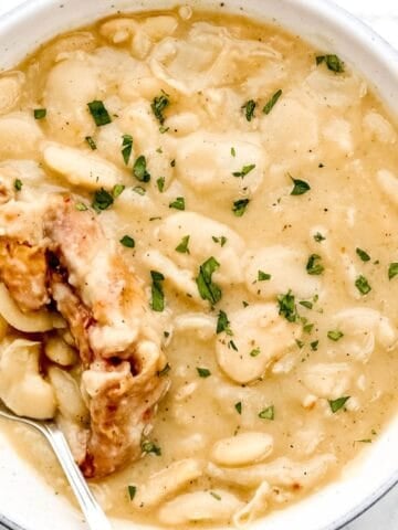 Overhead view of bowl of lima beans with meat and a spoon in it.