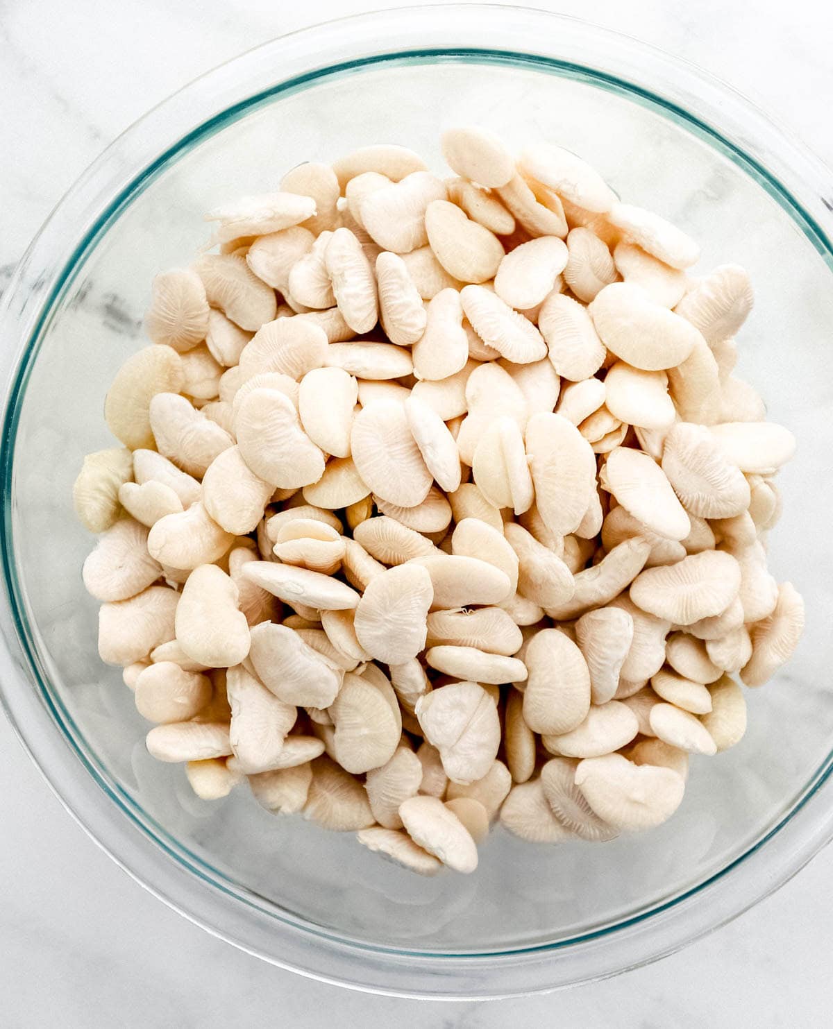 Soaked and drained lima beans in glass mixing bowl.