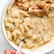 Overhead view of bowl of beans with spoon in it held by hand.