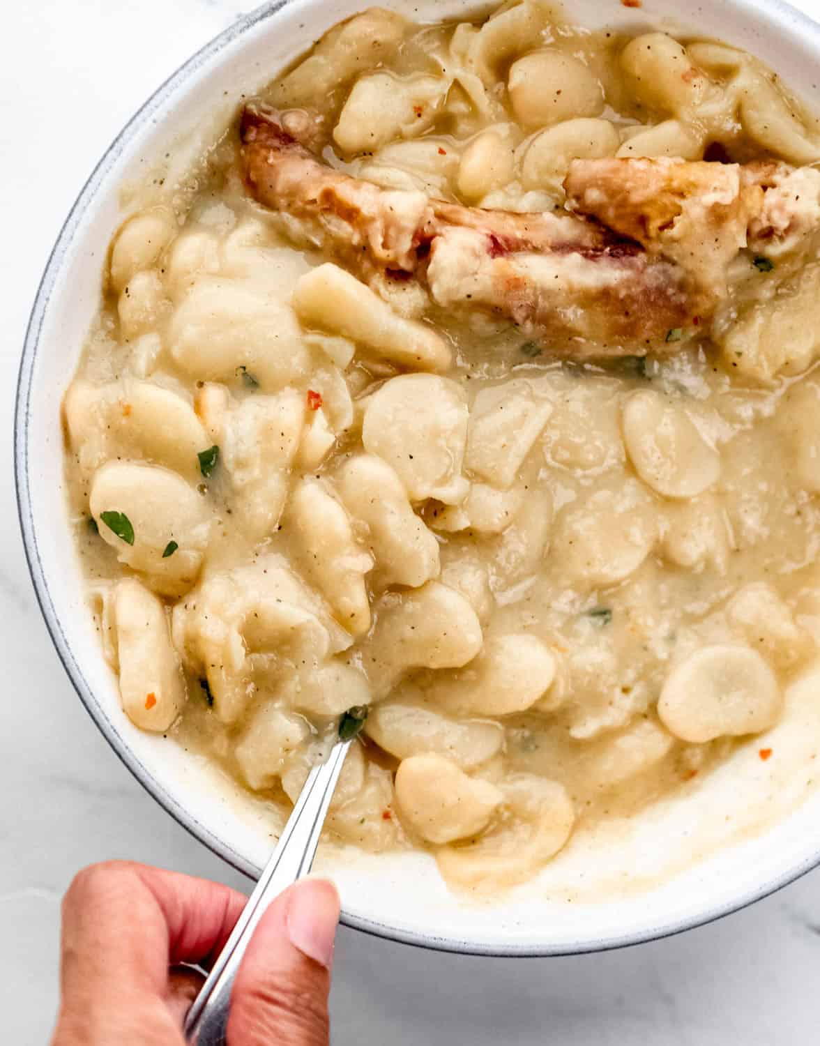Overhead view of bowl of finished beans with spoon in it held by hand.