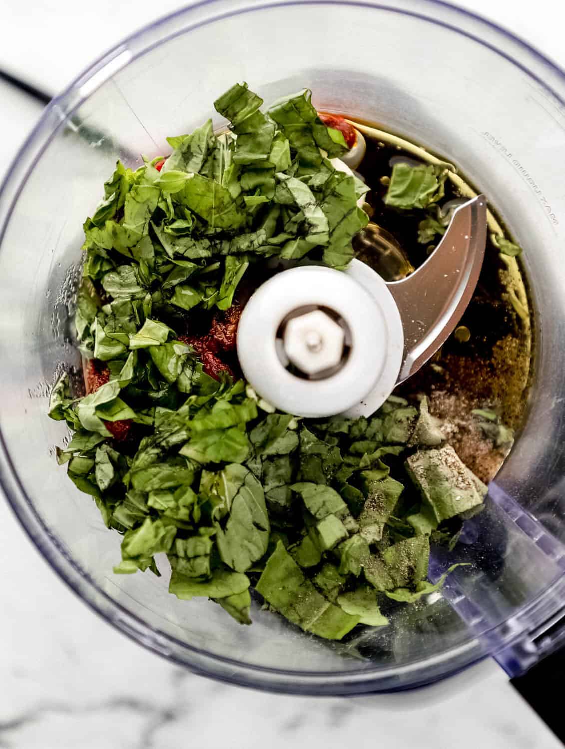 Overhead view of ingredients to make pesto added to food processor. 
