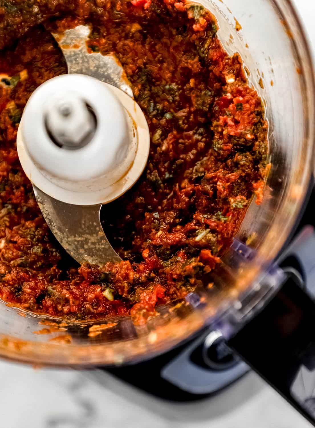 Close up view of pesto ingredients combined in food processor. 