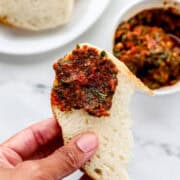 Close up of hand holding piece of bread with pesto on it.