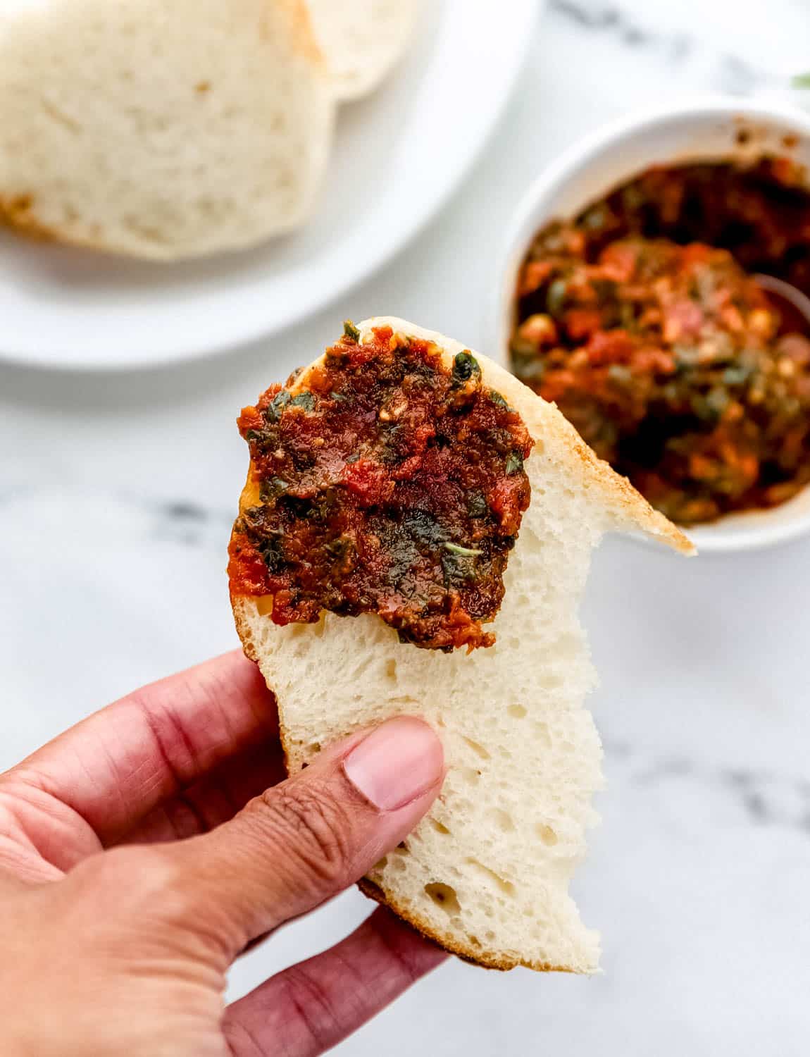 Hand holding piece of bread with finished pesto on it. 