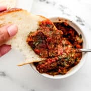 Close up view of hand holding piece of bread dipping into bowl of pesto.