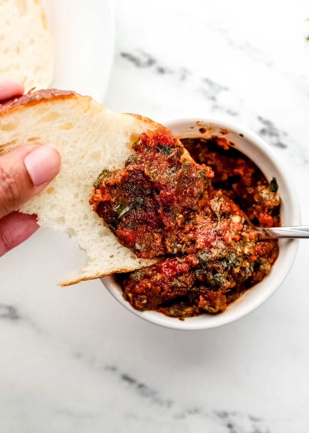 Close up view of hand with bread dipping into bowl of pesto. 