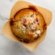 Overhead view of single muffin in liner on marble surface.