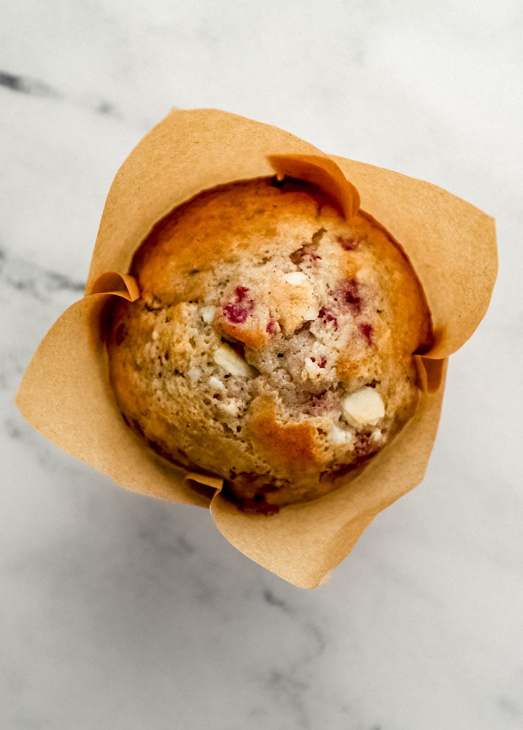 Overhead view of single muffin in liner on marble surface.