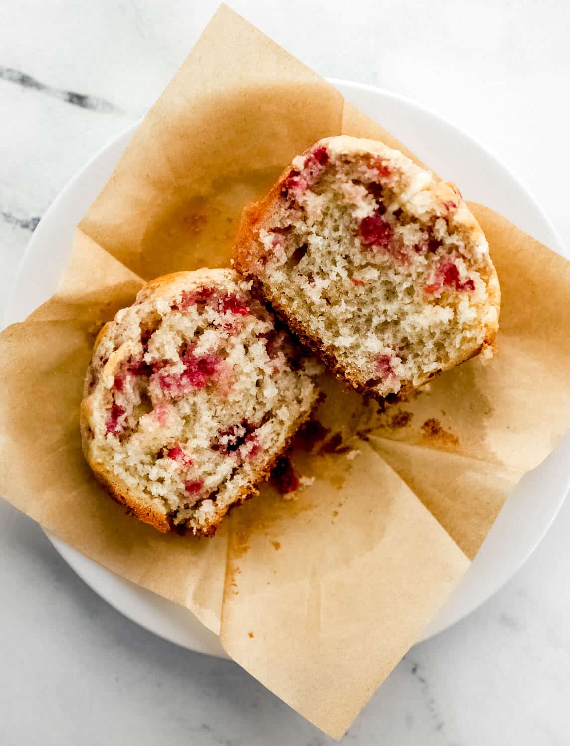 Overhead view of single muffin cut in half on top of brown muffin liner on plate.