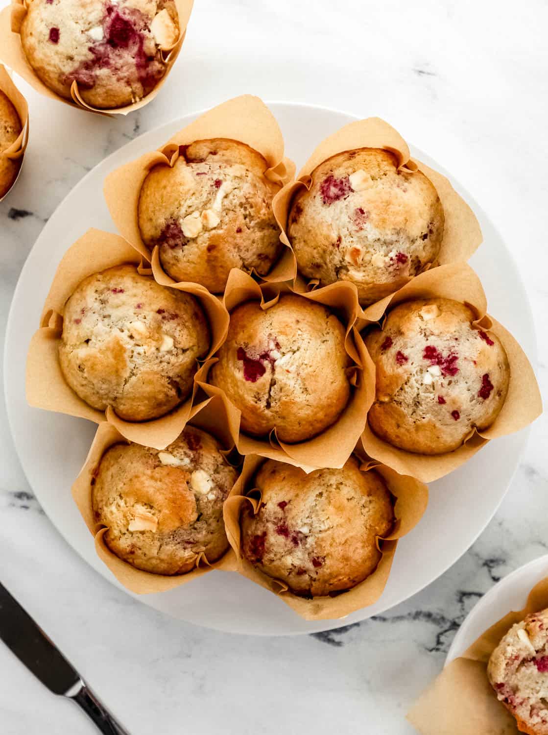 Overhead view of finished muffins on a white plate by a knife and other muffins.