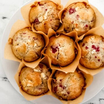 Overhead view of finished muffins on white plate on marble surface.