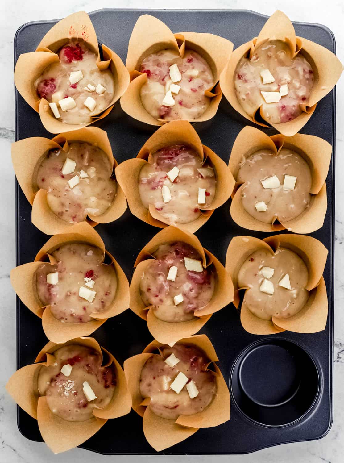 Overhead view of batter added to muffin pan inside muffin liners.