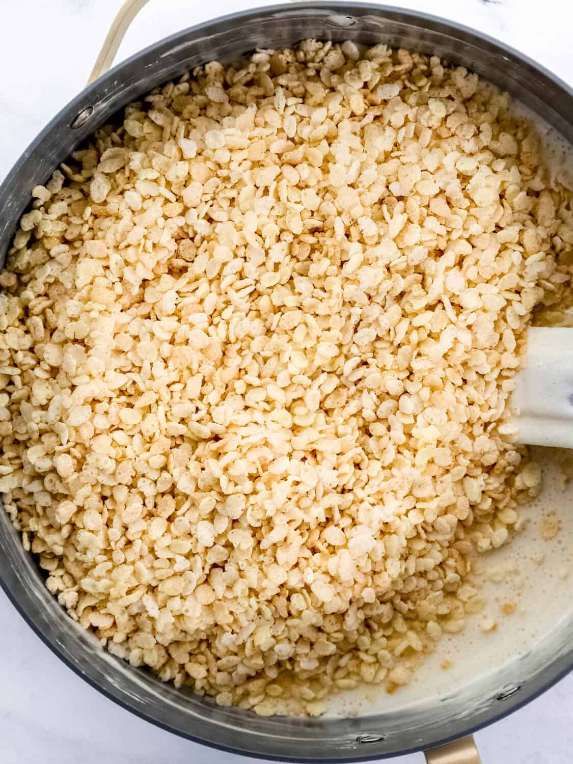 Cereal added to marshmallow mixture in large pot with spatula.