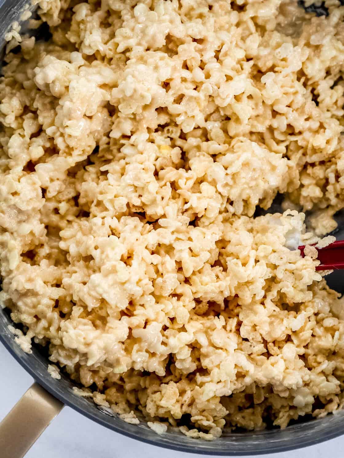 Rice krispie treats mixture in large pot being mixed with a spatula.