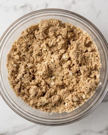 Overhead view of oatmeal and dry ingredients combined in glass mixing bowl.