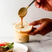 Close up view of hand holding spoon with sauce on it over a bun.