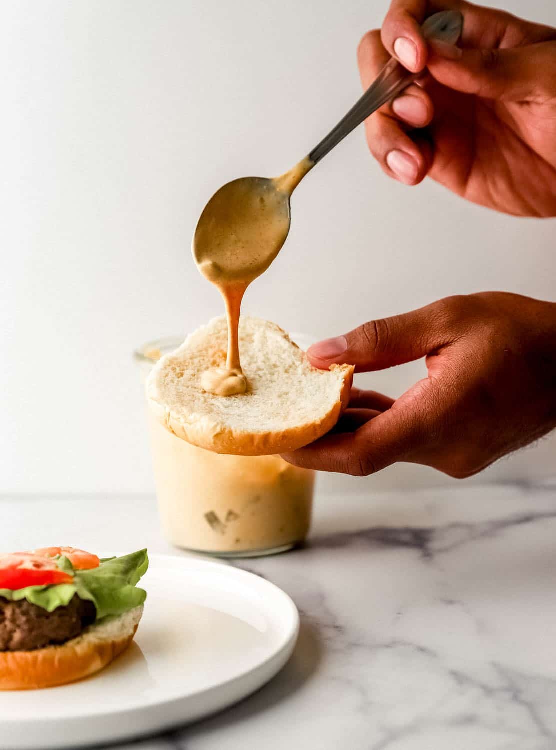 Close up view of hands adding sauce to bun using a spoon. 