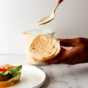 Hand holding burger bun spreading sauce with a spoon on it.