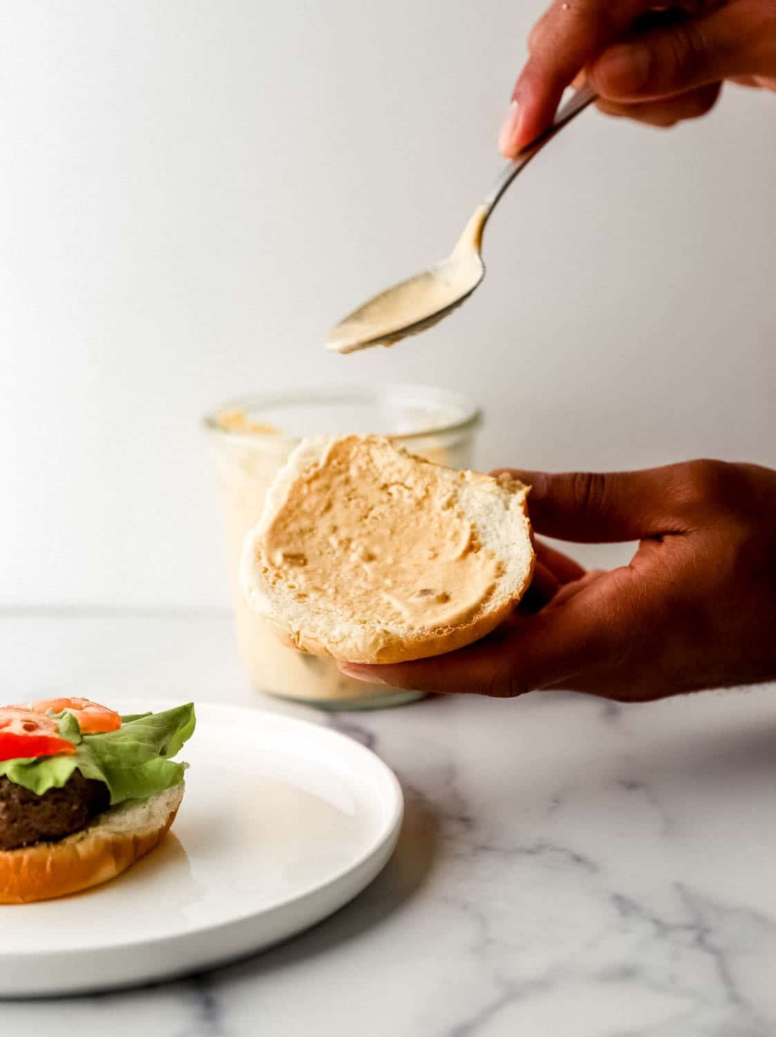 Hand holding burger bun with sauce spread on it. 