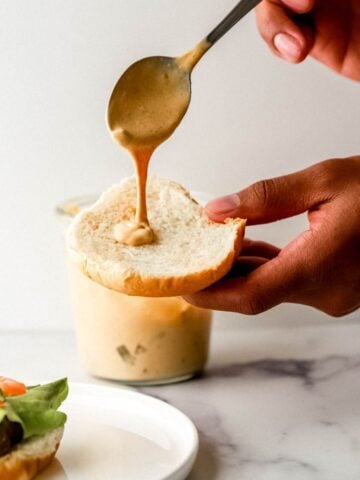 Close up view of hand holding bun and putting sauce on it with a spoon.
