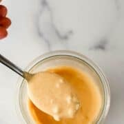 Photo of jar of sauce with hand holding spoon over it on pin with text overlay.