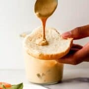 Photo of hand holding bun and putting sauce on it on pin with text overlay.