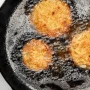 Overhead view of cast iron skillet with oil and tomatoes frying.