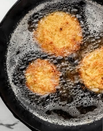 Overhead view of cast iron skillet with oil and tomatoes frying.