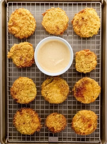 Tomatoes on wire rack sheet pan with small white bowl of sauce.