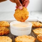 Close up side view of hand holding fried tomato over bowl of sauce.