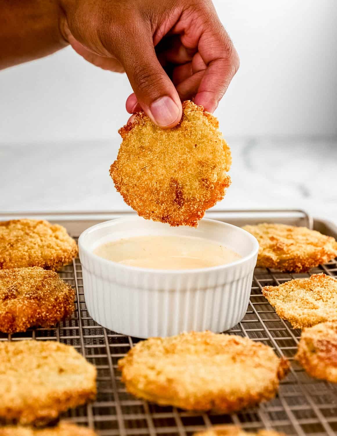 Close up view of hand holding fried green tomato over bowl of sauce. 