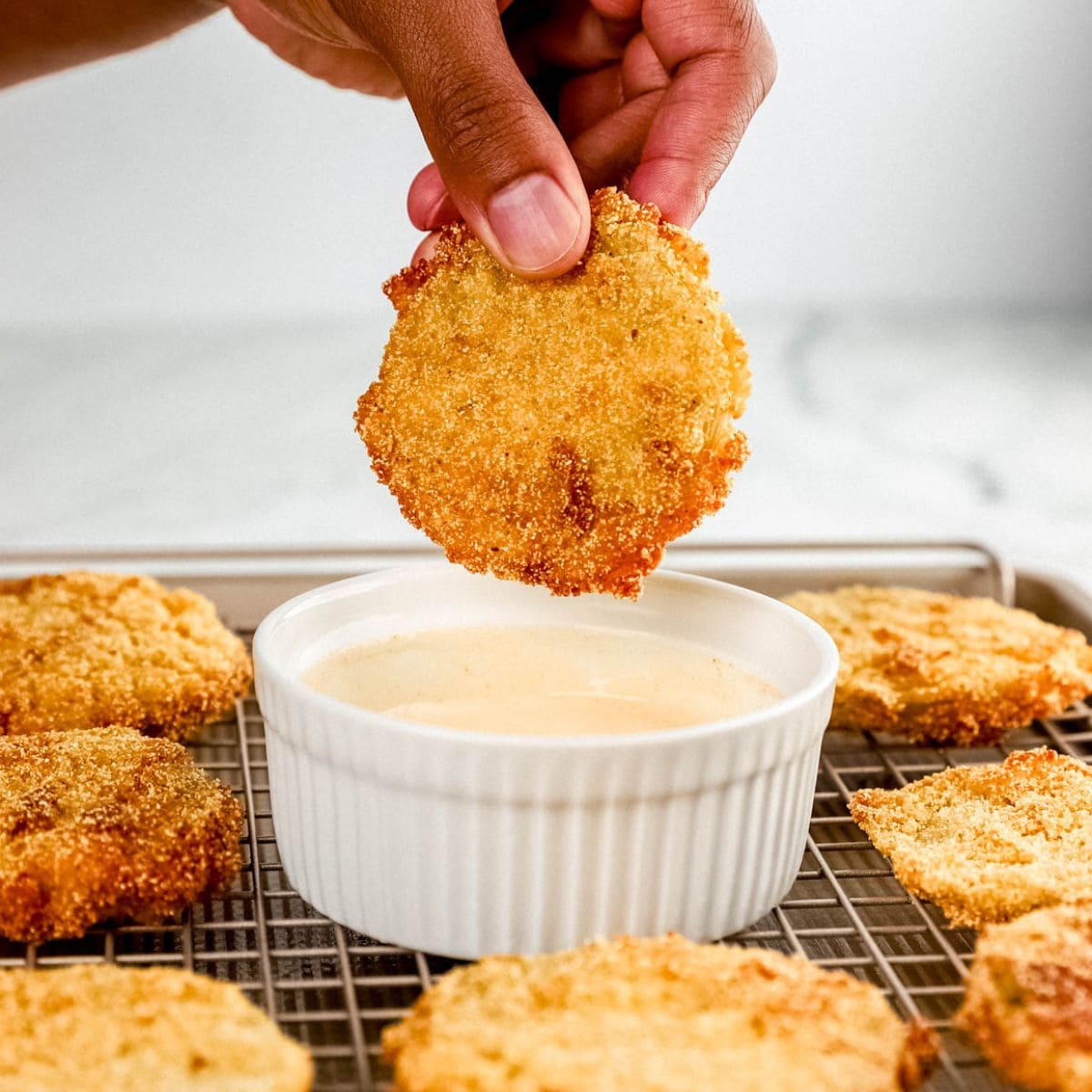 Side view of hand holding fried tomatoes over bowl of sauce.