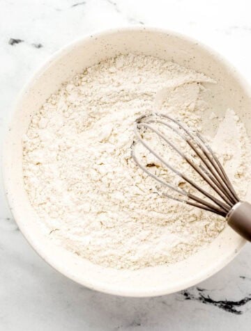 White bowl with flour and seasonings in it with a whisk.