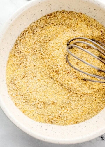 Overhead view of cornmeal and breadcrumbs combined in bowl with whisk.