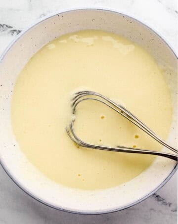 Overhead view of eggs and milk in bowl with whisk.