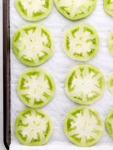 Overhead view of sliced tomatoes on paper towel lined sheet pan.