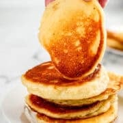 Stack of cakes on plate with a hand holding one on top.