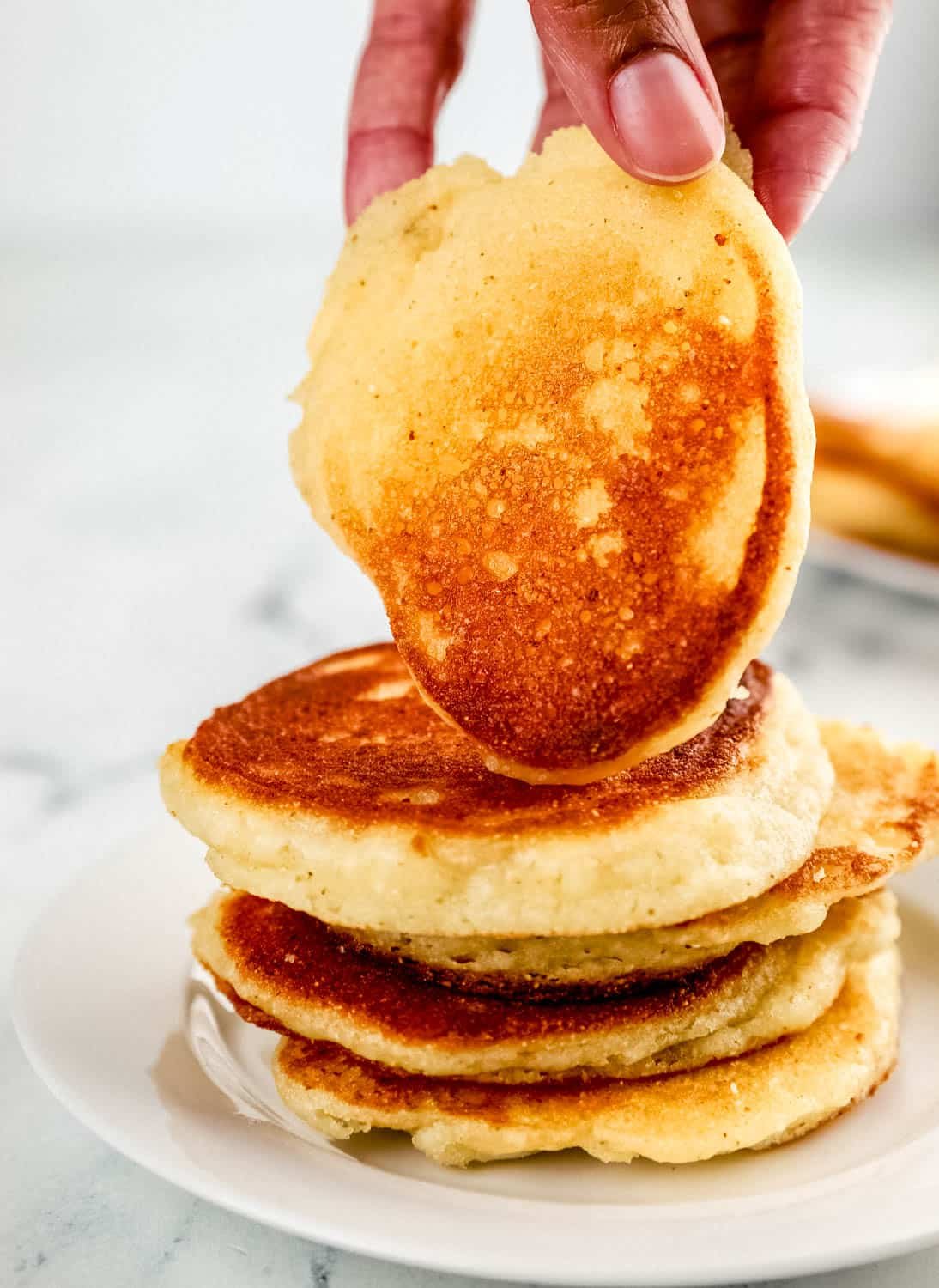 Close up side view of stack of hoe cakes on a plate with a hand holding one on top. 