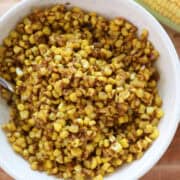 Overhead view of corn in a white bowl with spoon by fresh corn.