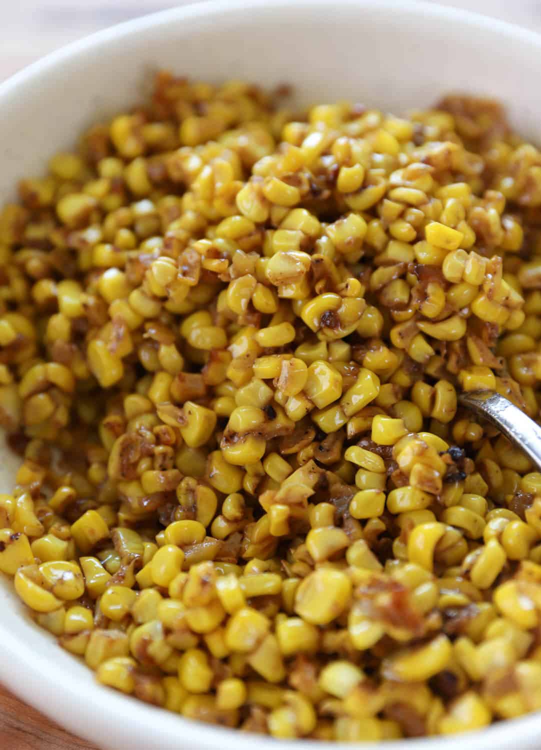 Close up view of corn in a white bowl with a spoon. 
