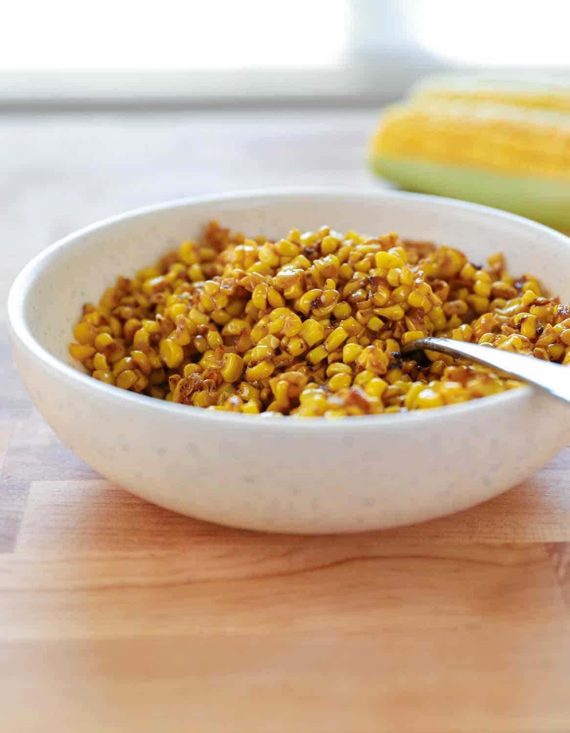 Close up side view of white bowl of corn with spoon in it on wooden surface. 