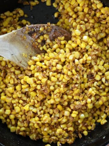 Close up view of fried corn in cast iron skillet with wooden spoon.