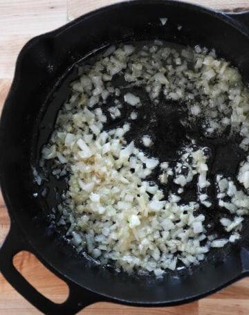 Overhead view of diced corn added to cast iron skillet with butter and oil.