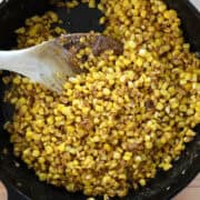 Overhead view of finished corn in a cast iron skillet with a wooden spoon.
