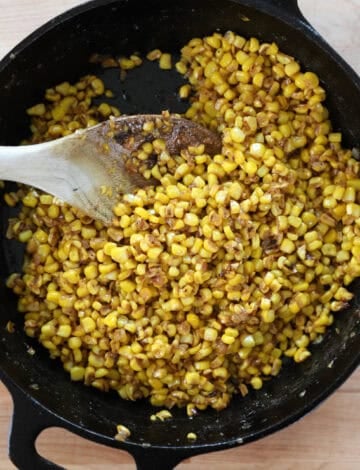 Overhead view of finished corn in a cast iron skillet with a wooden spoon.