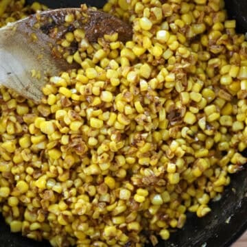 Close up view of fried corn in cast iron skillet with wooden spoon.