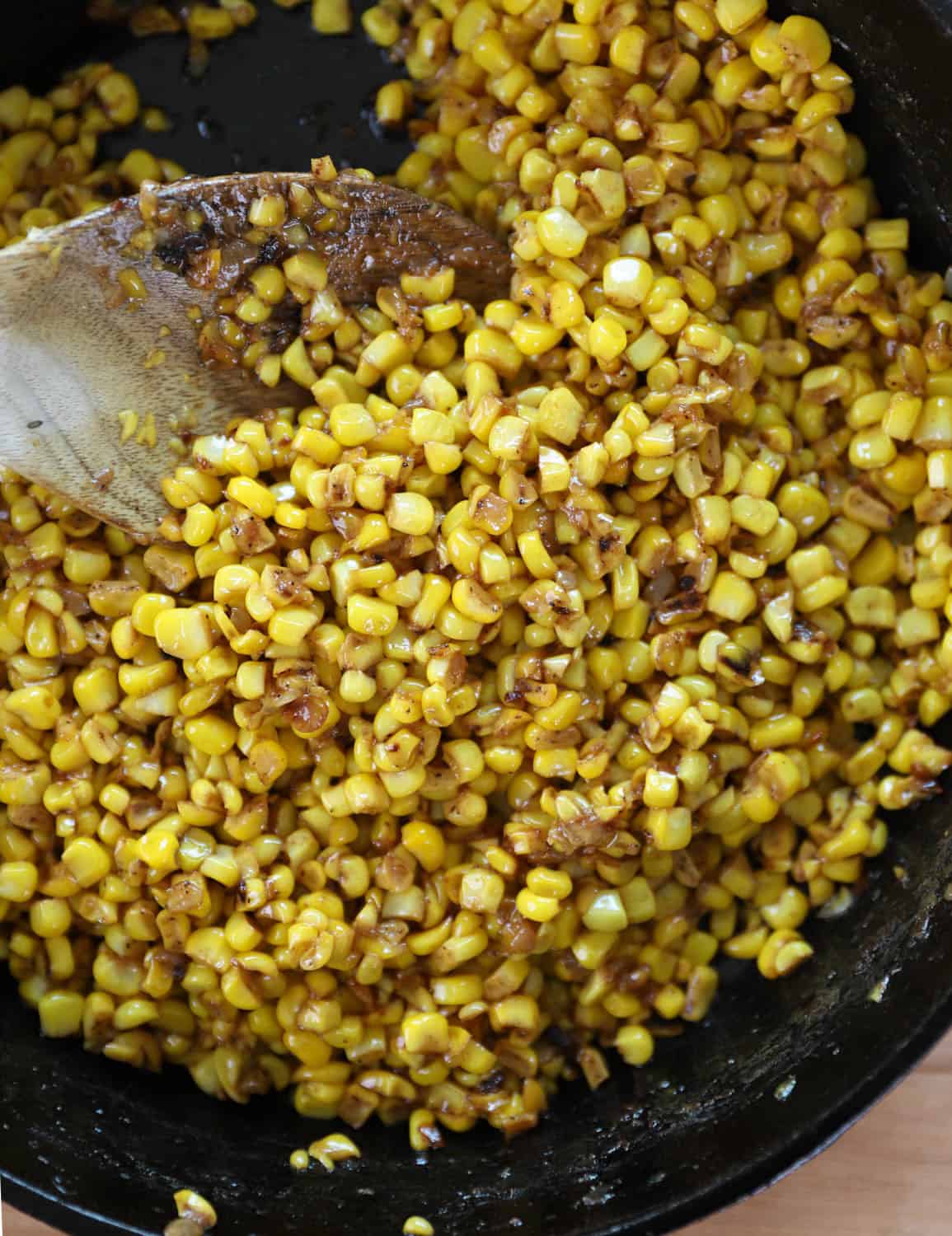 Fried corn in a cast iron skillet with a wooden spoon. 