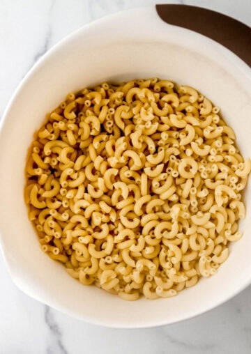 Overhead view of drained macaroni in large white mixing bowl.
